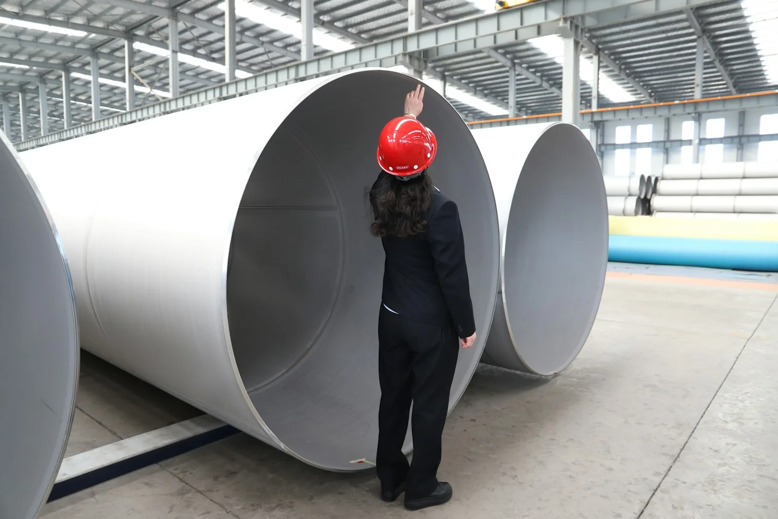 Persona con casco de seguridad junto a grandes conducciones de acero en una nave industrial